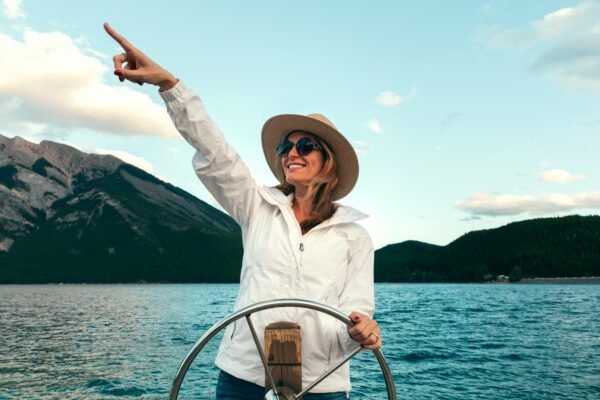 Smiling woman in a sun hat and sunglasses steering a boat on a mountain lake, pointing ahead