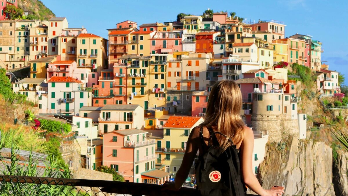 Woman with a backpack looking out over a colorful cliffside village on the Italian coast