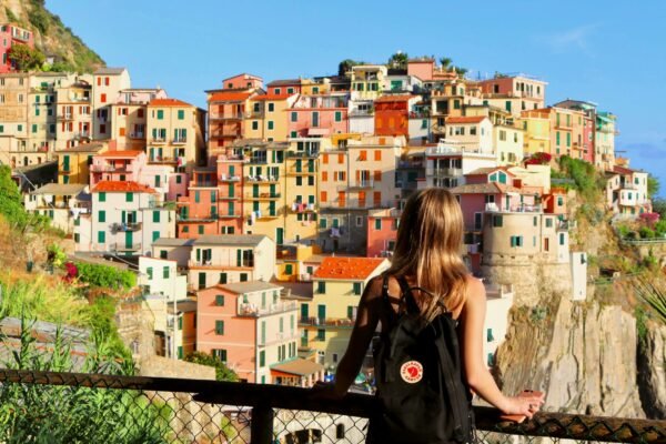 Woman with a backpack looking out over a colorful cliffside village on the Italian coast